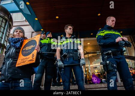 Un attivista XR incollato alle scale accanto alla polizia durante la campagna.Circa venti attivisti del gruppo Extinction Rebellion si sono presentati alla sede della Shell come parte della campagna Shell deve cadere, che si sta svolgendo per tutta la settimana in tutto il paese. Alcuni degli attivisti della ribellione d'estinzione si sono incollati alle finestre e alle porte di cristallo dell'edificio. Dopo aver rifiutato di lasciare il posto, la maggior parte di loro sono stati arrestati dalla polizia. Foto Stock