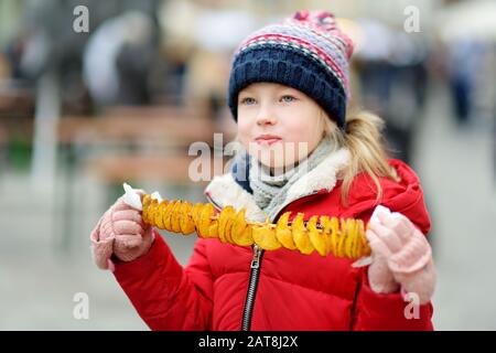 Ragazza carina mangiando patate fritte su un bastone freddo inverno giorno all'aperto. Spuntini per bambini. Foto Stock