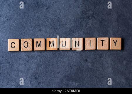 'Community' scritto in piastrelle di legno lettera su uno sfondo scuro e ruvido Foto Stock
