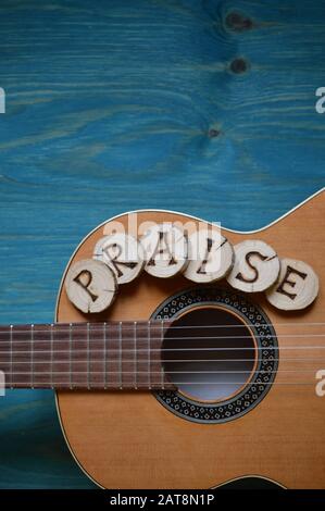 Chitarra su sfondo di legno teal con pezzi di legno su di esso scritta la parola: Lode Foto Stock