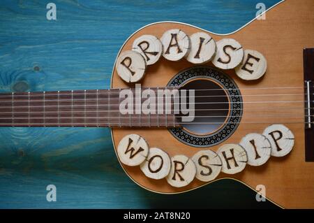 Chitarra su sfondo di legno teal con pezzi di legno su di esso lettere le parole: Lode e CULTO Foto Stock