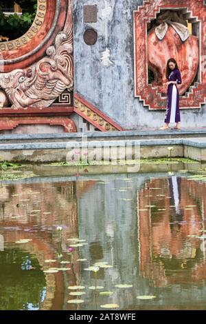 Ad Hoi An, Vietnam , l'agosto 2019 - la ragazza che riflette nella fontana della porta Tam Quan, o tre porte d'ingresso, che conduce al vecchio complesso del tempio bu Foto Stock