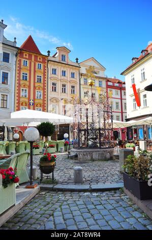Piccola piazza rotonda con una fontana nel centro della città con graziose case colorate contro il vibrante cielo blu al mattino. Praga, Repubblica Di Chezh Foto Stock