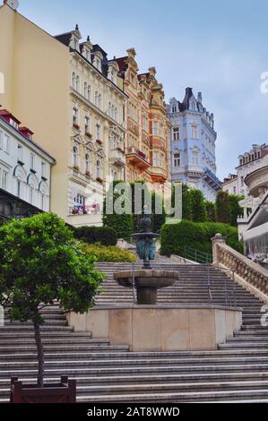 Scale di pietra che conducono ad una fontana nel centro della città con graziose case colorate contro il cielo blu durante il giorno Karlovy Vary, Repubblica di Chezh Foto Stock