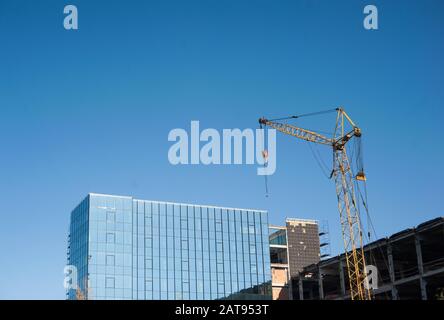 la gru a torre gialla costruisce un edificio in vetro contro un cielo blu Foto Stock