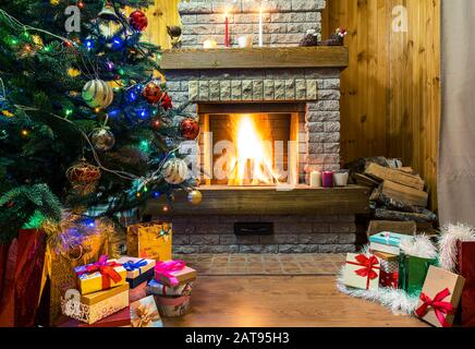 Natale sera. Albero di Natale e scatole regalo di natale e candele prima accogliente camino bruciante. Foto Stock