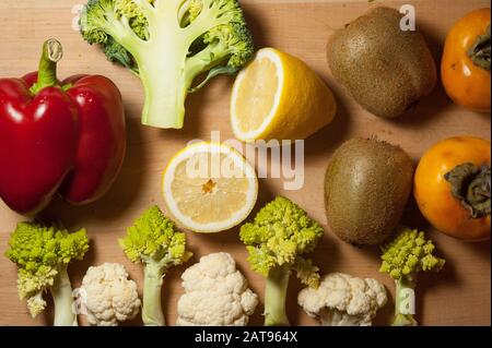 verdure e frutta su tavola di legno composizione: persimmoni, kiwi, limone, romanesco, broccoli, cavolfiore, peperone Foto Stock