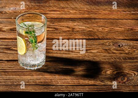 Carbonare acqua fredda con ghiaccio e limone scenda lungo ombra sul tavolo di legno Foto Stock
