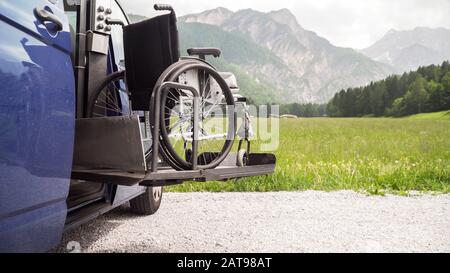 Foto dell'ascensore elettrico nero veicolo specializzato per disabili. Sedia a rotelle vuota su una rampa con la natura e le montagne sul retro Foto Stock