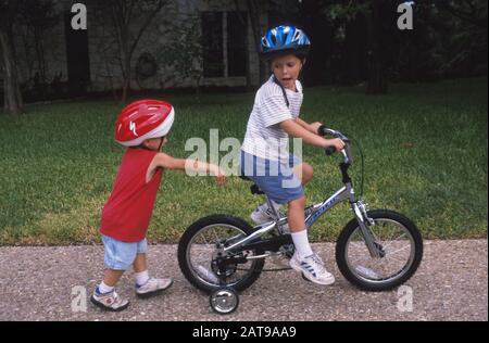 Austin, Texas: 5 anni di ragazzo in bicicletta con ruote da allenamento, mentre 3 anni fratello cammina dietro. ©Bob Daemmrich Foto Stock