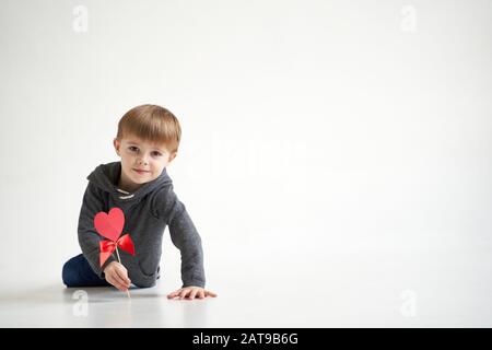 Dolce ragazzo che tiene il cuore di carta rossa su sfondo bianco. San Valentino o bambini salute, concetto medico Foto Stock