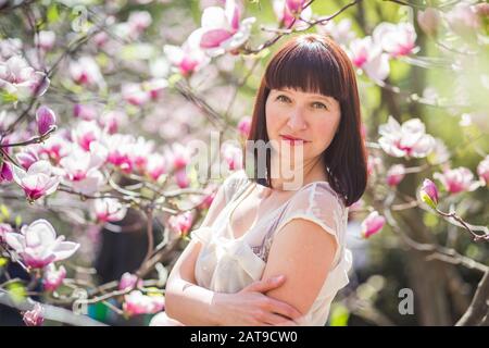 Bella dai capelli scuri donna tra i rami della magnolia. primi fiori in alberi in primavera. Foto Stock