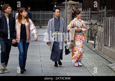 Due giovani adolescenti (uomo e donna) indossano un kimono in strada a Kyoto, vicino ad una giovane coppia vestita in stile occidentale moderno. Foto Stock