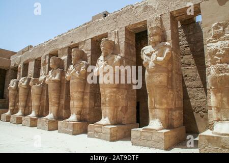 Luxor, Karnak, Egitto, Africa. Tempio di Karnak. Una fila di statue stand guardia all'interno del tempio mortuario di Ramses III. Foto Stock