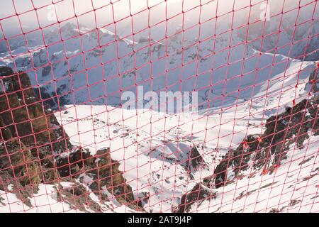 Rete di sicurezza ai margini di un crinale di montagna in inverno, con vista sul Passo Pordoi sottostante e la strada tortuosa, in Dolomiti, Alto Adige, Ita Foto Stock