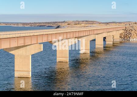 Ponte Stringer che si estende su un lago tranquillo con vista su terra nevosa e cielo nuvoloso Foto Stock