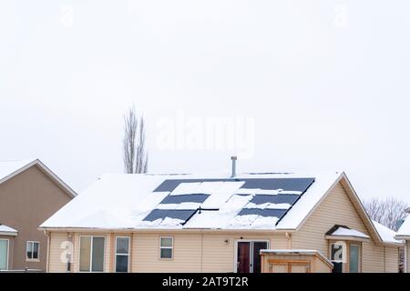 Tetto coperto di neve di casa con pannelli solari contro cielo nuvoloso in inverno Foto Stock