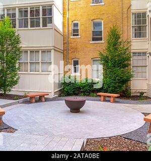 Panchine di pietra quadrata intorno ad un pozzo di fuoco fuori di un edificio residenziale in una giornata di sole Foto Stock