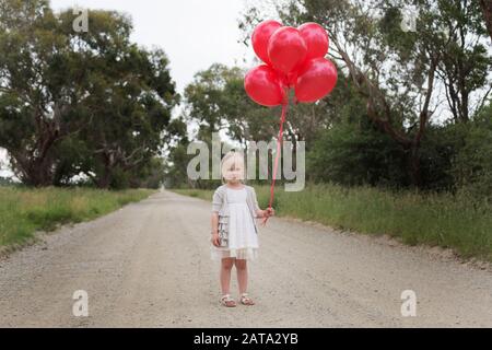 Australiana caucasica ragazza in piedi su una strada sterrata nel paese che tiene palloncini rossi Foto Stock