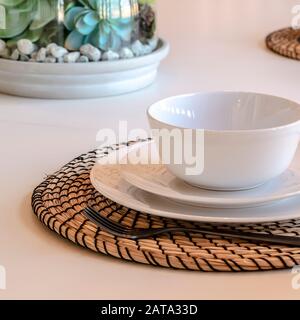 Cornice quadrata Foto piatto a ciotola e utensili su tavola rotonda contro tavolo da pranzo bianco Foto Stock