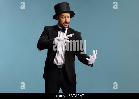 Mago maschio che esegue un trucco con le mani isolate su sfondo blu Foto Stock