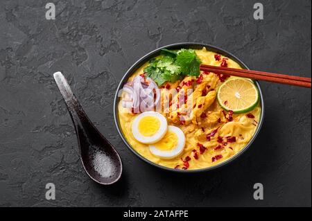 Ohn No Khao Swe in ciotola nera su fondo di ardesia scura. OH No Khao Suey è Coconut Latte Noodle Soup di myanmar cucina con carne di pollo e uova. Bur Foto Stock