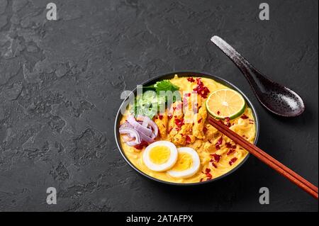 Ohn No Khao Swe in ciotola nera su fondo di ardesia scura. OH No Khao Suey è Coconut Latte Noodle Soup di myanmar cucina con carne di pollo e uova. Bur Foto Stock