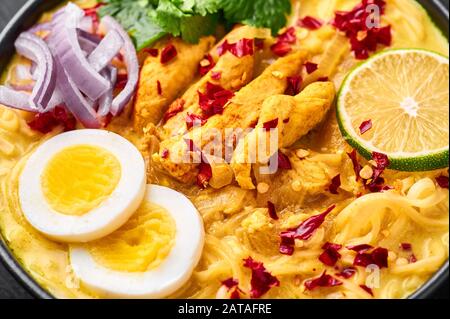 Ohn No Khao Swe in ciotola nera su fondo di ardesia scura. OH No Khao Suey è Coconut Latte Noodle Soup di myanmar cucina con carne di pollo e uova. Bur Foto Stock