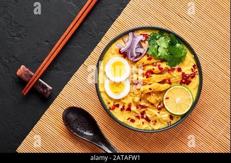 Ohn No Khao Swe in ciotola nera su fondo di ardesia scura. OH No Khao Suey è Coconut Latte Noodle Soup di myanmar cucina con carne di pollo e uova. Bur Foto Stock