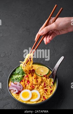 Ohn No Khao Swe in ciotola nera su fondo di ardesia scura. OH No Khao Suey è Coconut Latte Noodle Soup di myanmar cucina con carne di pollo e uova. Bur Foto Stock