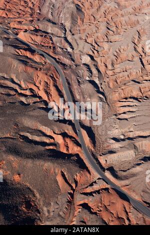 VISTA AEREA. Strada tortuosa in un paesaggio di badlands rosse e grigie. Nevada meridionale, USA. Foto Stock