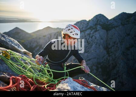 Un alpinista che bende il suo compagno con una corda verde dalla cima della montagna a Paklenica, in Croazia. Foto Stock