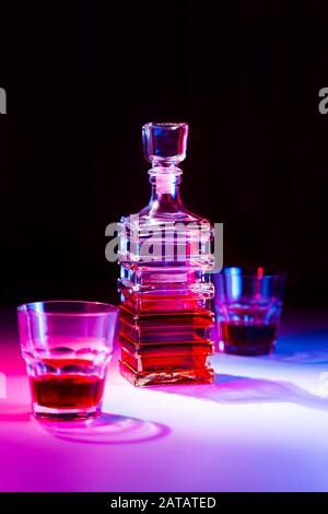 Caraffa quadrata in vetro con liquore con due bicchieri di vetro su tavolo bianco e sfondo nero. Foto Stock