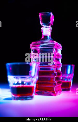 Caraffa quadrata in vetro con liquore con due bicchieri di vetro su tavolo bianco e sfondo nero. Foto Stock