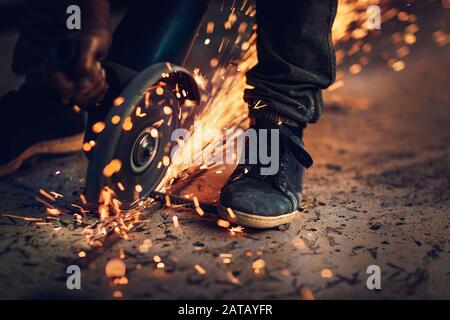 Saldatrice al lavoro, foto di closeup di scintille calde e luminose volano fuori da sotto la saldatura, duro lavoro, operai del collare blu Foto Stock