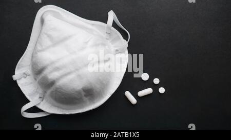 Concetto di epidemia e virus - pillole e maschere bianche su sfondo nero Foto Stock