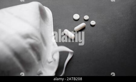 Concetto di epidemia e virus - pillole e maschere bianche su sfondo nero Foto Stock