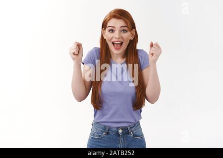 Eccitato allegro redhead studentessa allietata per il team universitario, rooting per amico, clench fisti stupito, sorridente gioioso, guardando la macchina fotografica Foto Stock