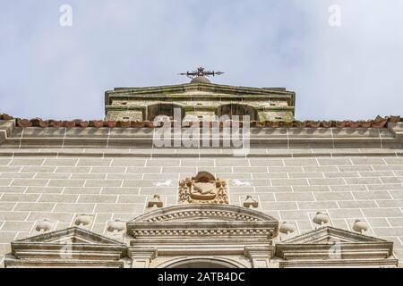 Campanile di una chiesa con una croce di metallo in cima e dettagli scolpiti in pietra sulla facciata, a ovest della Spagna, a Serradilla (Caceres) Foto Stock