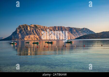 Isola Tavolara, barche, vista all'alba dalla Spiaggia di Cala Suaraccia, spiaggia del Mar Mediterraneo vicino al villaggio di Monte Petrosu, Sardegna, Italia Foto Stock