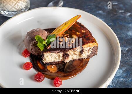 Dessert al cioccolato con una tazza di gelato al caffè, fette di ciliegia secca e una fetta di arancia. Guarnita con foglie di menta. Cappuccino nel backgr Foto Stock