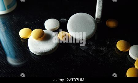 Concetto farmaceutico e medico su sfondo nero. Pillole mediche. Medicina e droghe. Molte pillole compresse gialle e capsule bianche Foto Stock