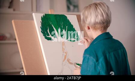 Una giovane donna bionda disegna un albero usando vernici Foto Stock