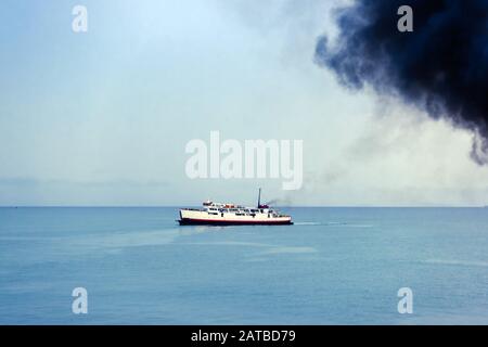 Tubo di scarico di traghetto con fumo nero spesso in uscita e cielo con nuvole sullo sfondo. Inquinamento atmosferico. Foto Stock