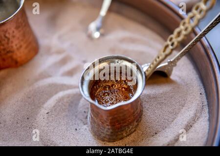 Tradizionale caffè turco in cezve preparato su sabbia calda. Messa a fuoco selettiva. Foto Stock