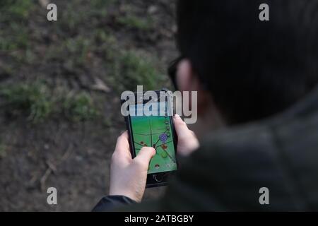 Un ragazzo dai capelli scuri di 12 in occhiali gioca a Pokemon Go Walking su un dispositivo mobile iPhone Foto Stock