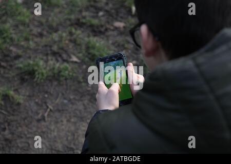 Un ragazzo dai capelli scuri di 12 in occhiali gioca a Pokemon Go Walking su un dispositivo mobile iPhone Foto Stock