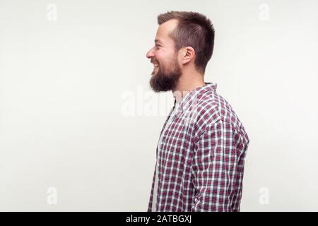 Ritratto di vista laterale di uomo felice bearded in camicia plaid casual sorridente sinceramente, soddisfatto soddisfatto con la vita, luogo vuoto per testo dell'annuncio, copia spazio. Io Foto Stock