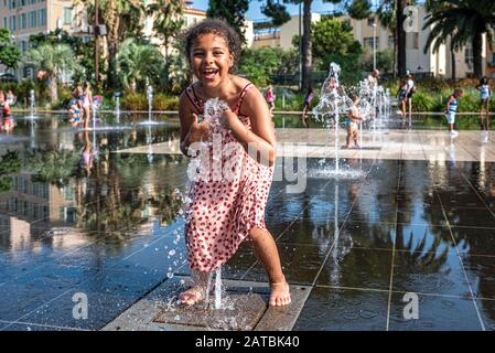 Il bambino si diverte con uno dei getti d'acqua che si trovano nel Mirroir d'eau sul nuovo luogo urbano, la Promenade du Paillon a Nizza, Francia Foto Stock