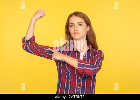 Guarda, sono donna forte! Ritratto della ragazza di zenzero auto-fiducioso in camicia casual che punta a bicipite, sensazione di potere ed energia per raggiungere il successo, orgoglioso Foto Stock